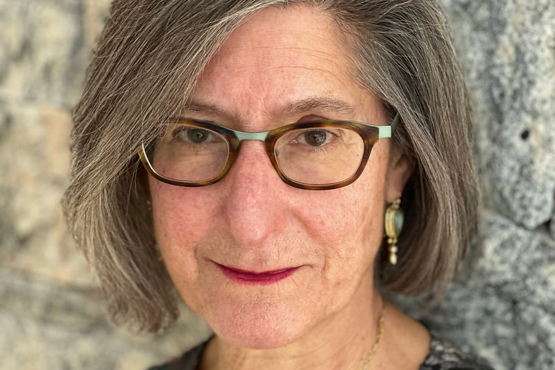 Woman with gray hair and glasses standing against a stone wall.