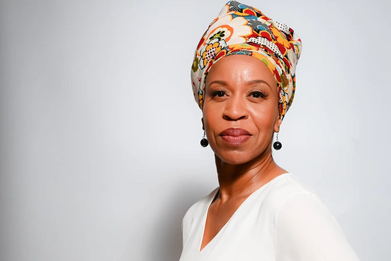 Woman wearing a bright head scarf and a white top against a white background